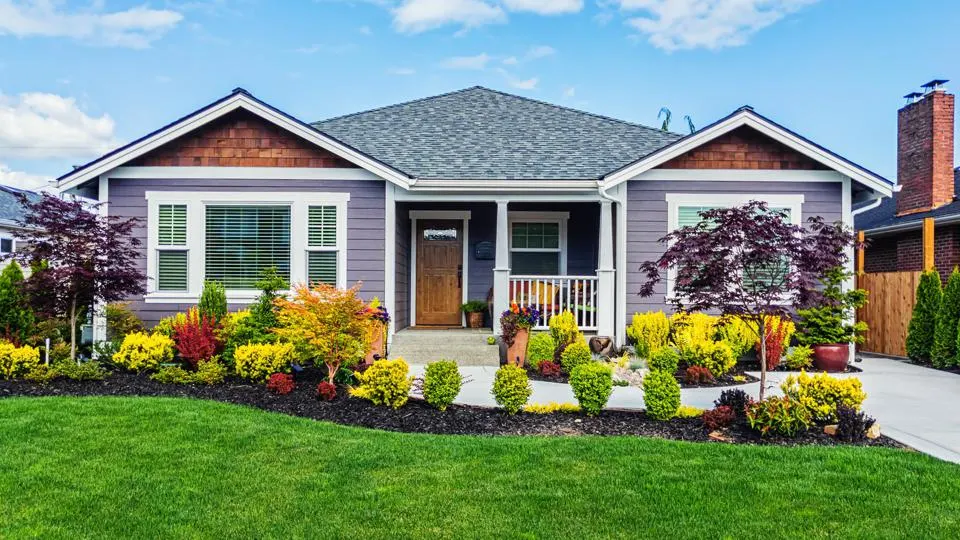 A charming single-story house with a gray exterior and a wooden front door, located in an area known for exceptional landscaping in Metro Louisville, Ky