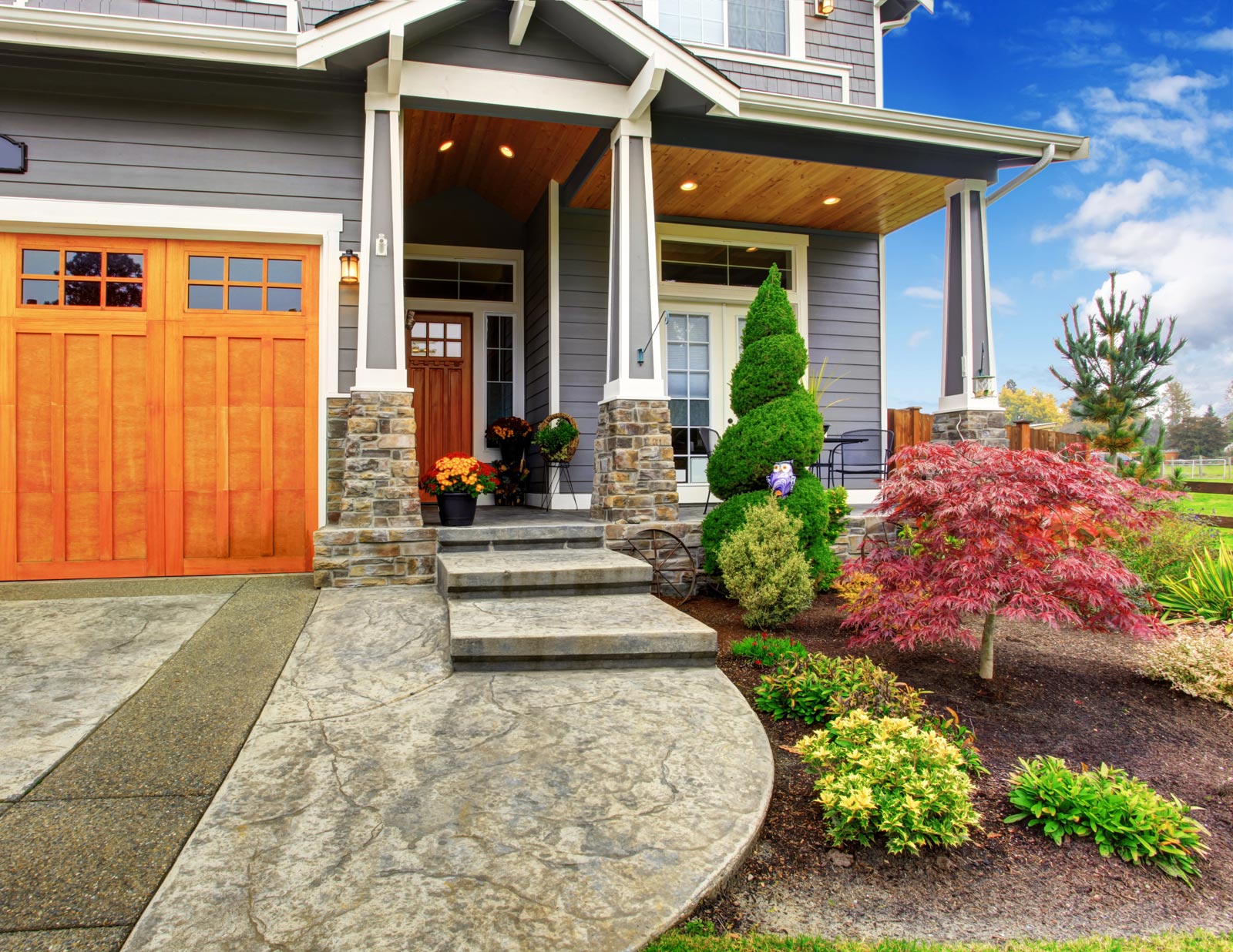 Modern house in Middletown, KY, gray siding, wooden front door, stone steps, potted plants, manicured landscaping. Red Japanese maple tree, green shrubs, clear blue sky, welcoming atmosphere.